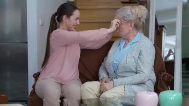 Neşeli olumlu milenyum kadını şaşırmış yaşlı emeklinin gözlüklerini çıkarıyor ve kontak lens takıyor. Kafkasyalı büyükannemiz, Bakıcı torunundan Kadınlar Günü hediyesi aldığı için mutlu. .