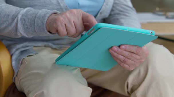 Közelkép, idősebb női kezek, amint tablettákat görgetnek a nappaliban. Felismerhetetlen magabiztos kaukázusi nyugdíjas nő szörfözés interneten online mobil app otthon. Öregedés és technológiák. — Stock videók