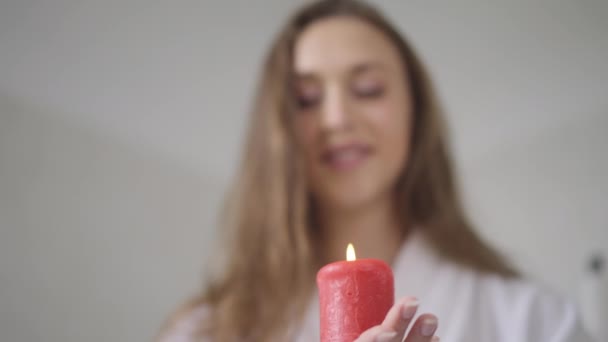 Detailní červená hořící svíčka v štíhlé ženské ruce s rozmazanou bělošskou brunetkou, která se usmívá na pozadí. Bezstarostný šťastný mladá dáma těší víkendový volný čas v koupelně doma. Zpomalený pohyb — Stock video