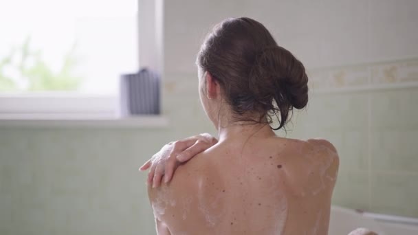 Visszapillantás meztelen vékony fiatal kaukázusi nő mosás vállak szappanhab lassított felvételen. Barna érzéki karcsú hölgy vigyáz a testbőrre otthon, a fürdőszobában. Nőiesség és higiénia. — Stock videók