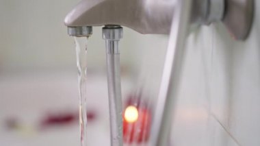 Banyodaki musluk, küvette akan su ve arka planda yanan bulanık mum. Otelde ya da evde köpükle dolu romantik bir banyo. Romantizm ve temizlik kavramı.