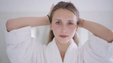 Yüzünde yamalar olan, at kuyruğunu kameraya baktıran güzel, sıska genç bir kadın. Evde yüz derisi ile ilgilenen ince, beyaz bir bayanın portresi. Sabah güzellik rutini.