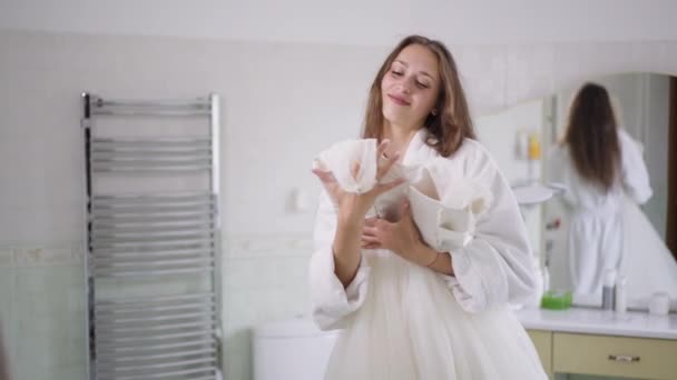 Feliz jovem noiva dançando com vestido de noiva em câmera lenta no banheiro em casa. Retrato de mulher caucasiana encantadora confiante que gosta de preparações de casamento dentro de casa. Conceito de feminilidade. — Vídeo de Stock