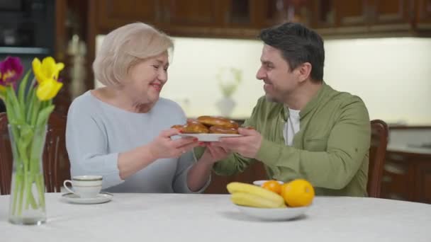 Dankbare volwassen zoon knuffelende oudere moeder lachend pratend dankend voor heerlijk gebakken dessert. Portret van een gelukkige blanke man die thuis in het weekend een ontmoeting heeft met een gepensioneerde vrouw. — Stockvideo