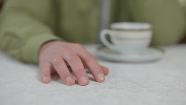 Ruka netrpělivého nervózního bělocha poklepávající prsty na stůl uvnitř. Nerozpoznatelný muž čeká myšlení s šálkem čaje doma. — Stock video