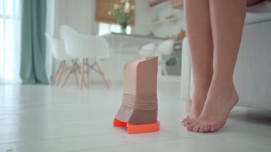 Kıdemli bir kadın giymeye hazırlanırken yerdeki bir yardım cihazının üzerine sıkıştırılmış çorap gerilir..