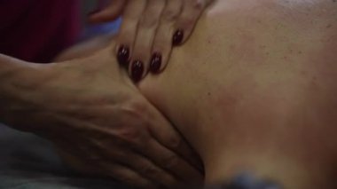 Yakın el kırmızıya boyanmış sırtında, Kafkas terapisti sıkı bir baskı uyguluyor. Avuç içleri yağlı ve baş parmaklı, kas düğümlerine ve gerilime odaklanmış, görülebilir.