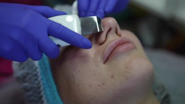 Genç bir kadın sivilce ve siyah noktalar için ultrasonik cilt temizleme tedavisi görüyor.