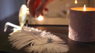 Beyaz bir tüyden gümüş bir kolye alan narin bir kadının yakın çekimi. Arka planda kokulu bir mum yanıyor