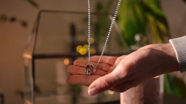 Yüzük kolyeli gümüş bir kolye tutan bir kadın eli, mum ışığında sıcak bir odaya düşürüyor. Duygusal an.