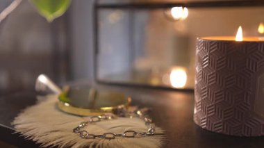 Kadın eli, tüyün üzerinde duran gümüş bir zincir bileziği alır. Yanan bir mumla samimi ve samimi bir atmosfer.