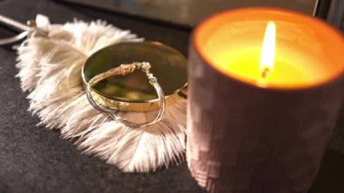 Yanan bir mum ve makrome dekorasyonun yanında gümüş bir bilezik tutan bir kadının yakın çekimi. Gece rutini için rahat bir atmosfer