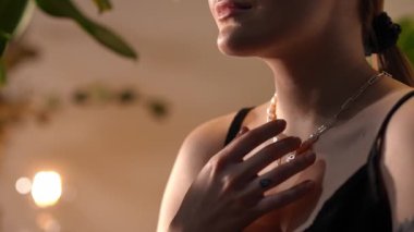 Genç kadın zarif bir inci ve gümüş zincirli kolyeye nazikçe dokunuyor. Göğsüne, boynuna ve ellerine yakın çekim yap.