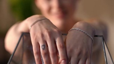 Küçük bir kalp dövmesi ve gümüş bilezikleri olan bir kadının elleri. Nazikçe dokunuyor ve cam akvaryuma dokunuyor.