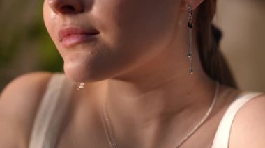 Çekici genç bir kadının boyun ve çene hattının yakın plan videosu. Küpesine ve tenine hafifçe dokunuyor, sıcak güneş ışığının tadını çıkarıyor.