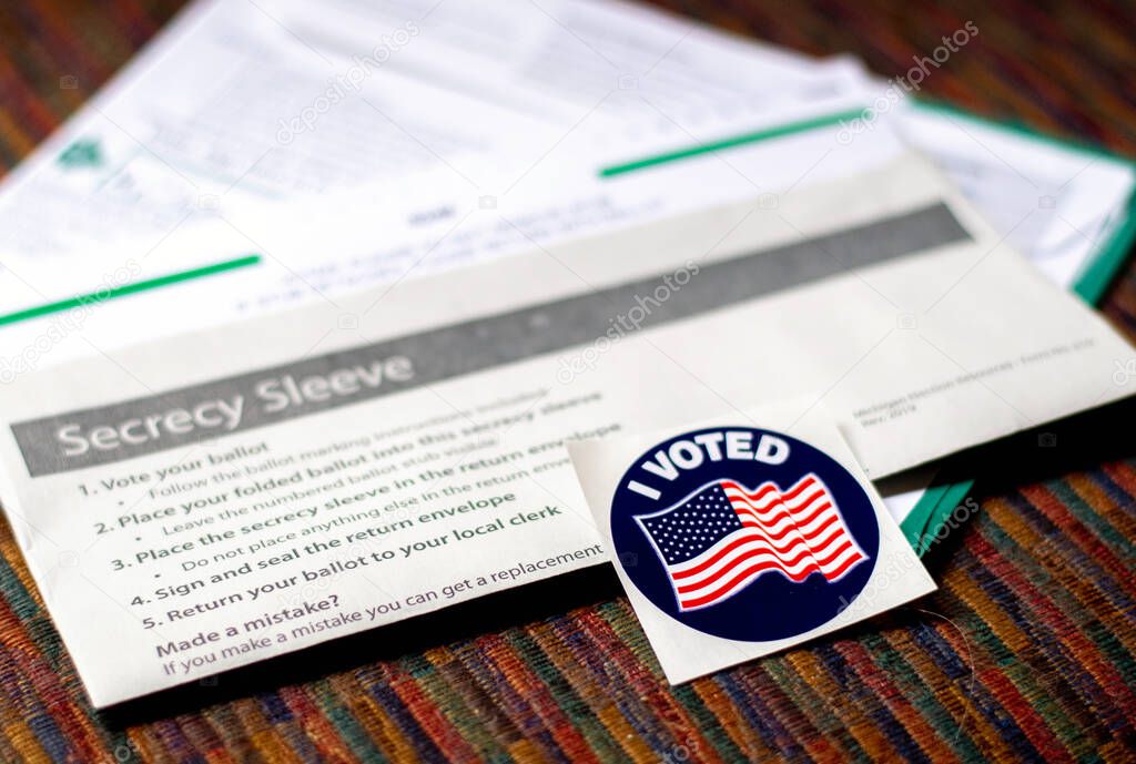 I voted sticker is set against a Absentee ballot and return envelope ready to mail in to cast my vote in America