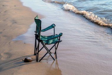 Michigan Gölü kıyısındaki ıslak kumda katlanan bir plaj sandalyesi duruyor.