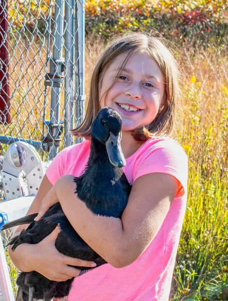 Smiling girl holds her pet duck as she poses outdoors with her animal