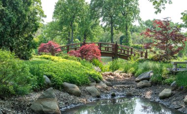 Güzel kemerli bir köprü bu güzel bahar parkındaki küçük bir nehri kaplar.