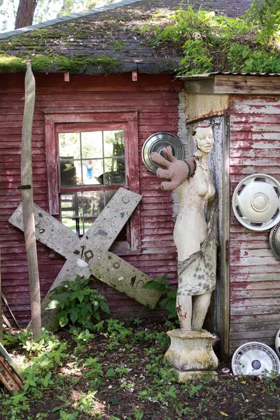 A worn out statue reaches out from the corner of a rustic barn, a humorous still life in this quirky ooutdoor antique shop
