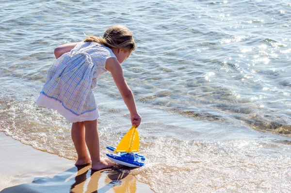 Menina brincando com veleiro de brinquedo no lago — Fotografia de Stock