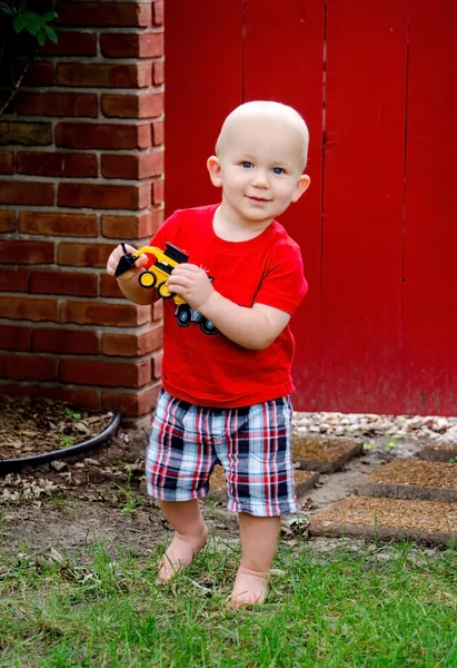 Toddler boy and toy truck by a red gate — Stock Photo, Image