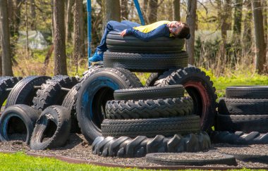 Çocuk, yerel bir oyun alanındaki büyük bir lastik kulesinin tepesinde dinleniyor.