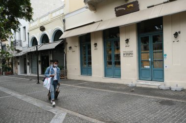 Yunanistan 'ın başkenti Atina' da 3 Kasım 2020 'de Covid-19 salgınının yayılmasına karşı yeni kısıtlayıcı tedbirlerin uygulanmasının ilk günü boyunca kapalı bir kafe önünde yürüyen bir yaya görülüyor.