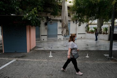 Yunanistan 'ın başkenti Atina' da 3 Kasım 2020 'de Covid-19 salgınının yayılmasına karşı yeni kısıtlayıcı tedbirlerin uygulanmasının ilk günü boyunca kapalı bir kafe önünde yürüyen bir yaya görülüyor.