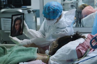 Tıbbi personelden biri, 5 Kasım 2020 'de Atina, Yunanistan' daki hastanenin yoğun bakım ünitesindeki akrabalarıyla yaptığı video görüşmesi sırasında COVID-19 Coronavirus hastasının önünde tablet tutuyor..