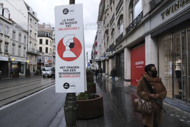 İnsanlar Brüksel, Belçika, 1 Aralık 2020 'de ticari bir caddede yüz maskesi takmaları gerektiğini hatırlatan bir tabeladan geçiyorlar.. 