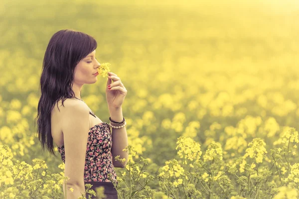 Mujer genuina en el prado de flores amarillas olfateando flor — Foto de Stock
