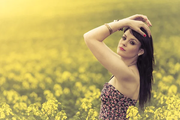 Schöne Frau auf einer Wiese aus gelben Blumen mit erhobenen Händen — Stockfoto