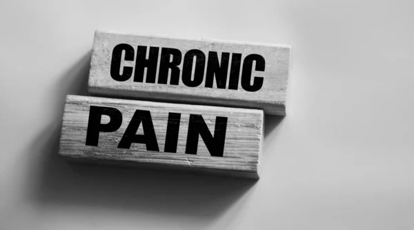 Chronic pain words on wooden blocks on pink with copyspace. Medicine healthcare concept.