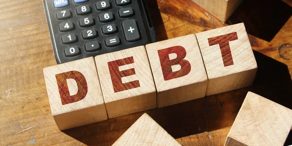 木制立方体上的债务词带有字母和木制背景上的计算器 金融和商业概念 — 图库照片