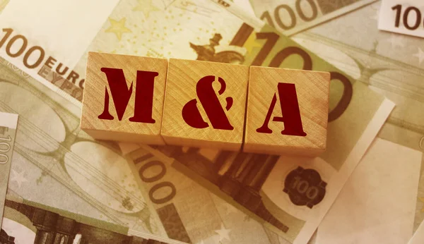 Mergers and acquisitions, M and A concept. Text on wooden cubes and cash in 100 euro bills.