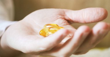 Yumuşak jel hapları ve Omega-3 yağı hap şişesinden sızıyor. Yakın plan, yaşlı bir kadının elinden. Sağlık sigortası konsepti. Seçici yemek.