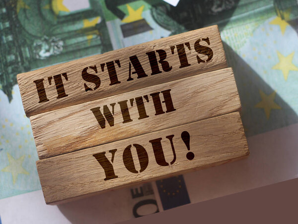 it starts with you, phrase written on vwooden blocks standing on 100 Euro bills. Professional skills and achievements concept. Personal Saving and investment concept.