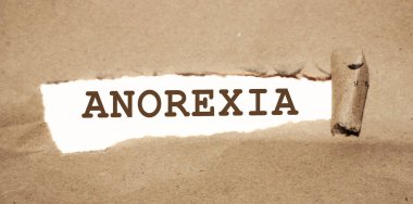 Kahverengi yırtık kağıdın arkasında anoreksi kelimesi beliriyor. Yeme bozuklukları kadın sağlık hizmetleri kavramı.