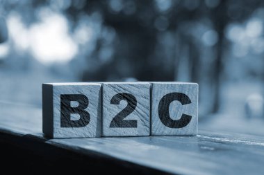 Tahta küplerdeki B2C harfleri dışarıda duran ahşap masaya konmuş. Yaz doğası geçmişi. Ticaretten müşteriye konsept. İstemci odaklı.
