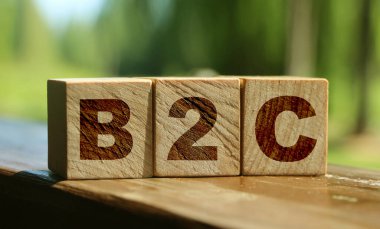 Tahta küplerdeki B2C harfleri dışarıda duran ahşap masaya konmuş. Yaz doğası geçmişi. Ticaretten müşteriye konsept. İstemci odaklı.