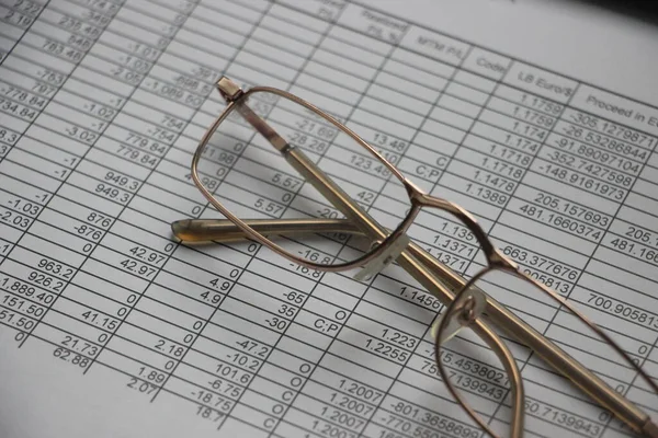 Worksheets or reports showing figures through eye glasses. Financial concept.