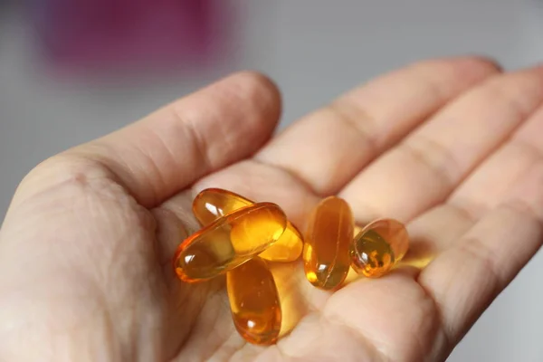 Medicine, nutritional supplements and people concept - close up of hands holding cod liver oil capsules. Hands of a woman holding fish oil Omega-3 capsules. Food supplements and healthcare concept.