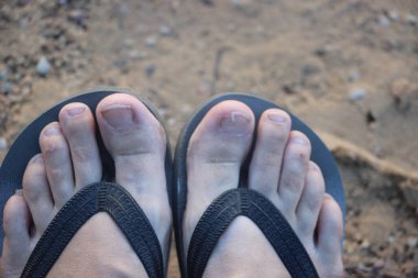 Sahilde sandalet giymiş ayakların görüntüsünü kapat.