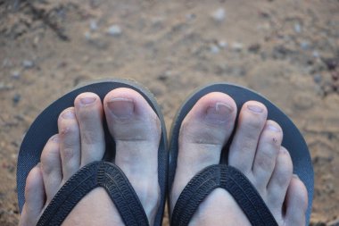 Sahilde sandalet giymiş ayakların görüntüsünü kapat.