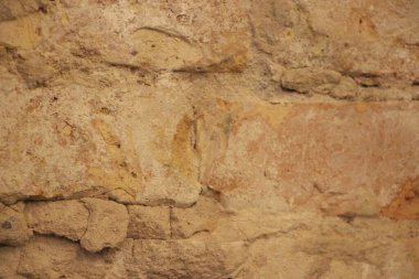 Dokulu kumlu bir duvarın yakın görüntüsü. Toprak tonları ve doğal desenleri var..