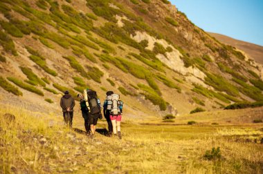 Bir grup yürüyüşçü dağ manzaralı kayalık geçitten yurt yerleşimine doğru iniyor. Sary Chelek Gölü, Sary-Chelek Celal Abad bölgesi, Kırgızistan, Orta Asya 'da yürüyüş yapan genç erkek ve kadınlar.