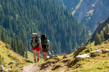 Bir grup genç yürüyüşçü dağlarda yürüyüş yapıyor. Yazın Sary Chelek Gölü, Sary-Chelek Celal Abad bölgesi, Kırgızistan, Orta Asya 'da seyahat eden iki erkek sırt çantasıyla geziyorlar..