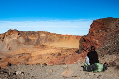 Young woman hiker with backpack sitting and looking at  desert near Pico del Teide mountain in El Teide National park. Tenerife, Canary Islands, Spain
