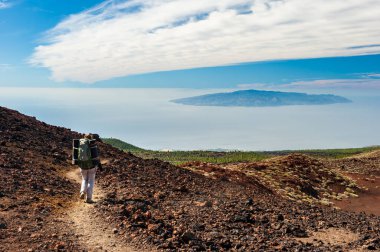 Canary Island La Gomera in sea and young woman hiker with backpack descending from Pico del Teide mountain in El Teide National park. Tenerife, Canary Islands, Spain